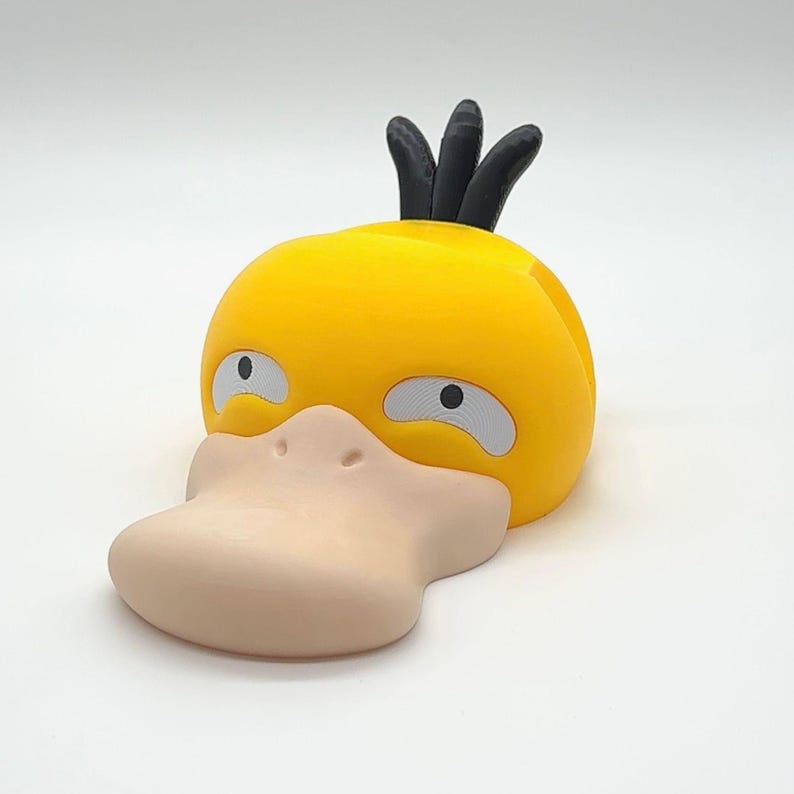 May include: A yellow, 3D-printed Psyduck figure with a light tan bill and eyes. The figure has three black spikes on top of its head. The figure is a collectible item.