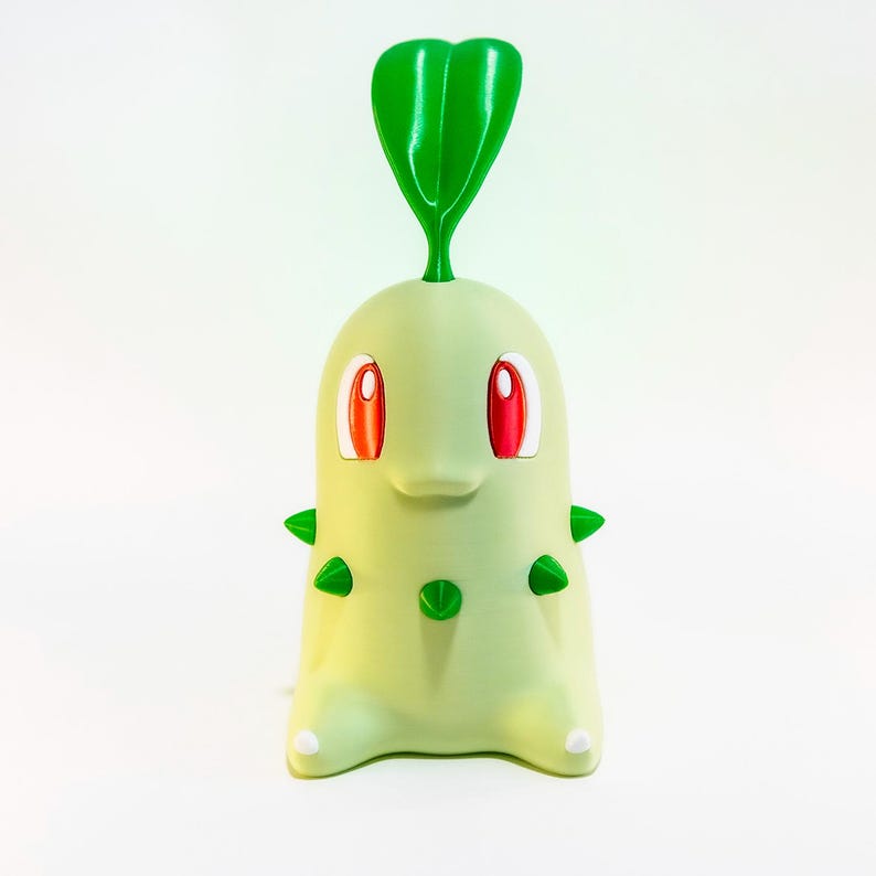 May include: A light green Chikorita figure with red eyes and green spikes. The figure has a large green leaf on top and small white feet. The figure is a collectible item from the popular Pok&eacute;mon franchise.