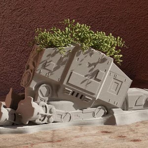 May include: A white ceramic planter shaped like a Star Wars AT-ST walker with green plants growing out of the top.