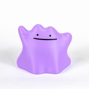 May include: A solid purple, blob-shaped figure with a simple, smiling face. The figure has a smooth, rounded form and a cheerful expression. The design is reminiscent of a popular character from a well-known animated series.