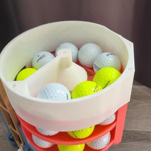May include: A golf ball cart filled with white and neon yellow golf balls. The cart is white and red, with multiple shelves for storage. The golf balls have the brand name "Titleist" printed on them.