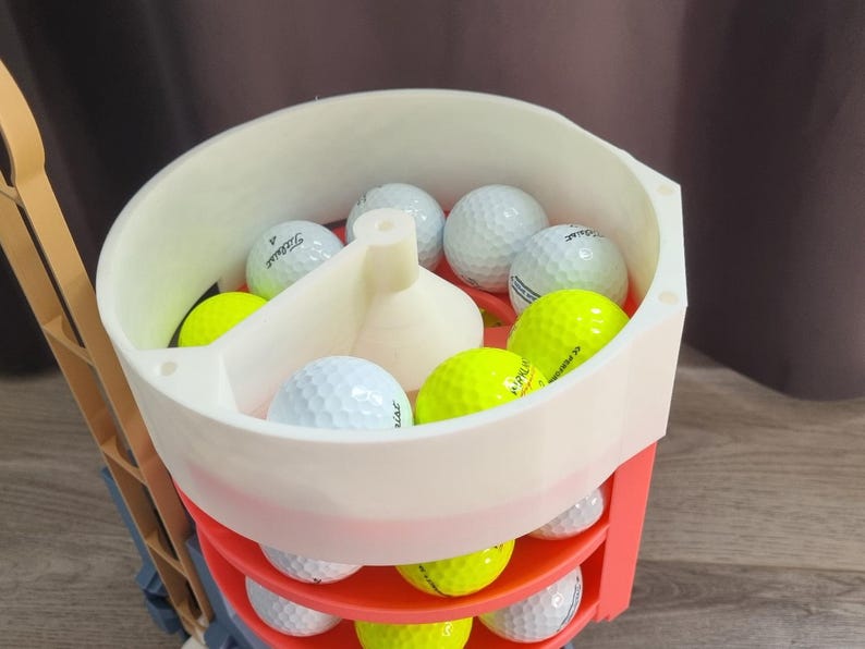 May include: A golf ball cart filled with white and neon yellow golf balls. The cart is white and red, with multiple shelves for storage. The golf balls have the brand name "Titleist" printed on them.