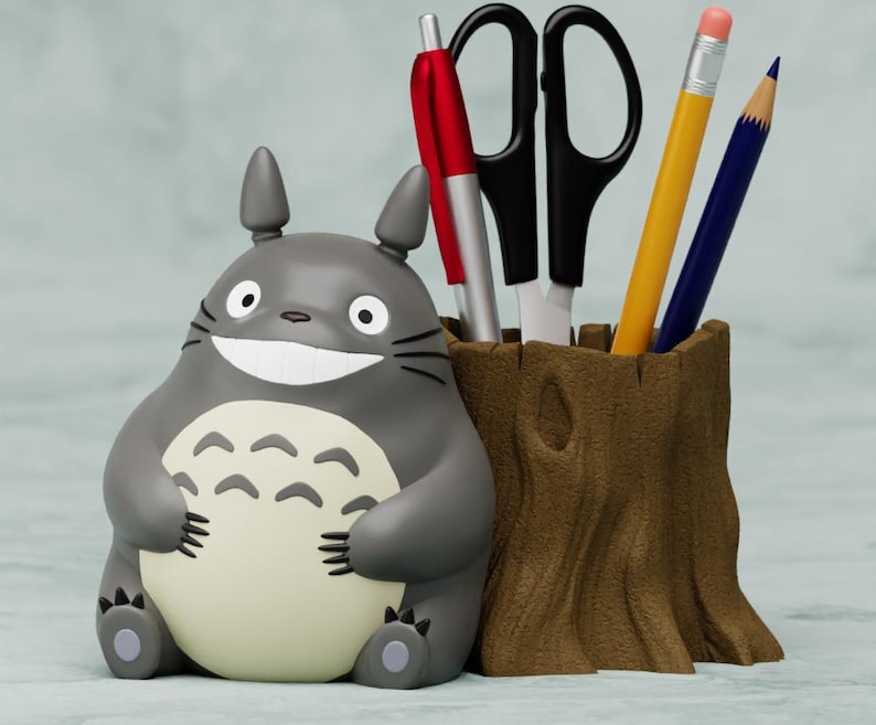 May include: A gray and white Totoro character desk organizer with a brown tree trunk base. The organizer holds a red pen, a silver pen, a pair of black scissors, a yellow pencil, and a blue pencil.