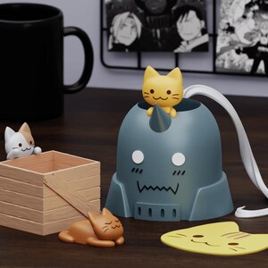 May include: A blue and gray figurine of a robot with a cat head, with a yellow cat figurine sitting on top. There are three other cat figurines, one white and two brown, on a wooden surface.