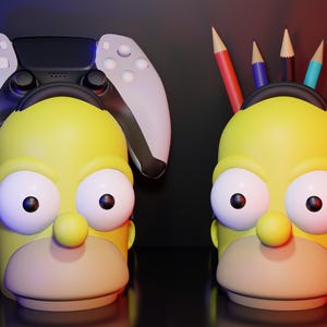 Könnte beinhalten: Zwei gelbe Schreibtisch-Organizer in Form eines Homer Simpson-Kopfes. Einer hält einen weißen und schwarzen Gamecontroller, der andere Buntstifte. Die Organizer haben große weiße Augen, eine kleine Nase und einen beigen Mund.