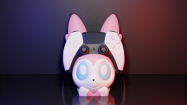 May include: A pink and white gaming controller holder shaped like a cartoon character with large ears. The holder is designed to cradle a black and white gaming controller. The background is a gradient of dark blue and red.