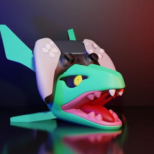 May include: A teal and pink dinosaur-shaped gaming controller stand. The stand has a wide open mouth with white teeth and a yellow eye. A black and white gaming controller is placed on top of the dinosaur's head. The stand has fins and a tail.