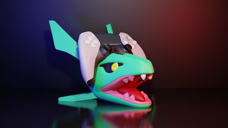 May include: A teal and pink dinosaur-shaped gaming controller stand. The stand has a wide open mouth with white teeth and a yellow eye. A black and white gaming controller is placed on top of the dinosaur's head. The stand has fins and a tail.