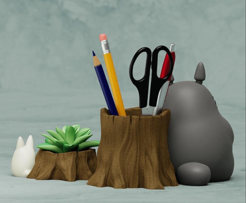 May include: A gray Totoro character figurine, a white Totoro figurine, and a brown wooden tree stump pencil holder with a green succulent plant. The pencil holder has two pencils and a pair of scissors inside.