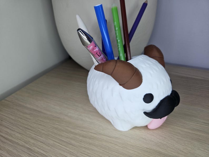 May include: White ceramic desk organizer shaped like a cartoon animal with brown horns, black mustache, and pink tongue. The organizer has multiple pens and pencils inside.