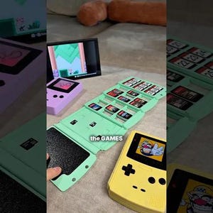 May include: A collection of retro handheld gaming consoles and game cartridges. The image features a yellow and a purple console, along with a green cartridge holder. The text "the GAMES" is visible on the green holder.
