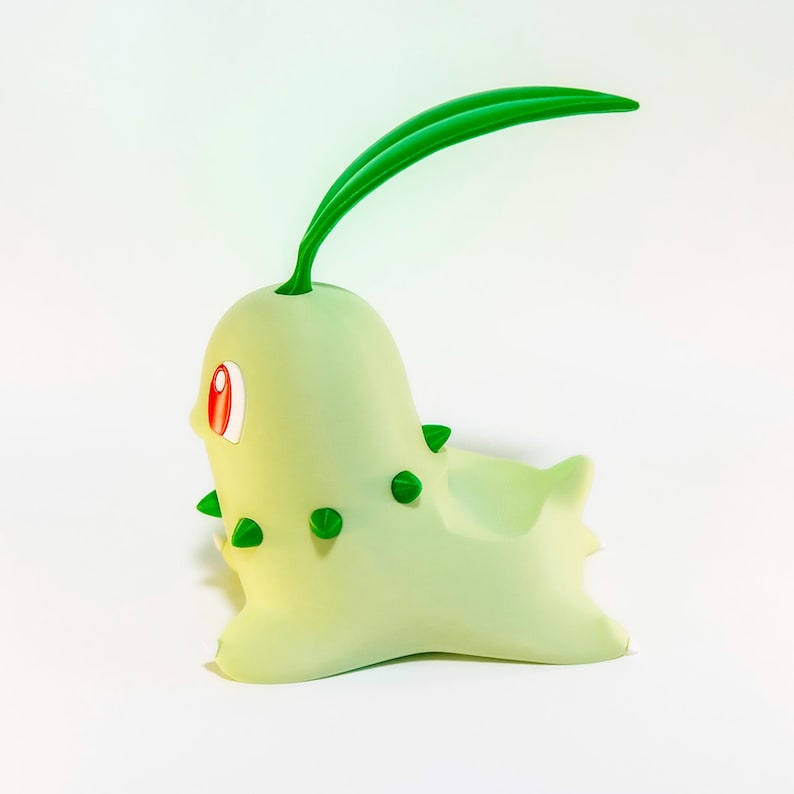 May include: A light green Chikorita figurine with a bulbous body, green spikes, and a long green leaf on its head. The figurine has red eyes and is set against a white background.