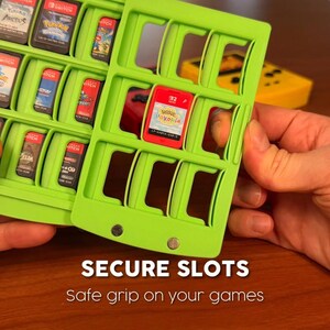 May include: Two bright green game cartridge holders with multiple slots, each holding a game cartridge. The text "SECURE SLOTS" and "Safe grip on your games" is displayed. A yellow game controller is visible in the background.