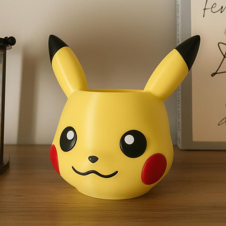 May include: A yellow Pikachu-shaped planter with black-tipped ears, black eyes, and red cheek circles. The planter has a wide opening for plants and is a decorative item for Pokemon fans.