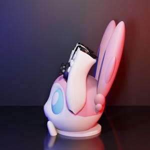 May include: A 3D-rendered figurine of a Sylveon character, featuring a white body, pink accents, and large, ear-like appendages. A black and white object is placed on top of the figurine. The background has a gradient of blue and red.