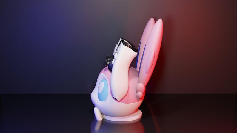 May include: A 3D-rendered figurine of a Sylveon character, featuring a white body, pink accents, and large, ear-like appendages. A black and white object is placed on top of the figurine. The background has a gradient of blue and red.