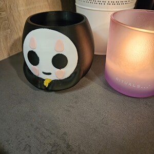 May include: Black and white ceramic planter shaped like a cartoon character with pink cheeks and black eyes. The planter is sitting on a brown surface.