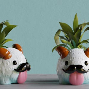 May include: Two white ceramic planters shaped like a furry creature with orange horns, black moustache, and pink tongue. Each planter has a green plant growing out of the top.
