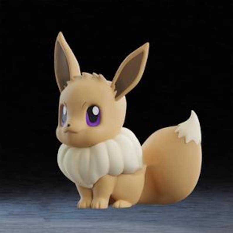 May include: A figurine of Eevee, a Pok&eacute;mon character, in a seated position. The figure is primarily tan with a white ruff, a fluffy tail with a white tip, and large, expressive eyes with purple pupils. The background is dark.