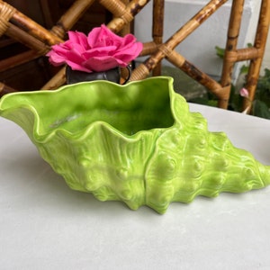 May include: A bright green ceramic planter shaped like a seashell. The planter has a textured surface and is perfect for displaying small plants or flowers.