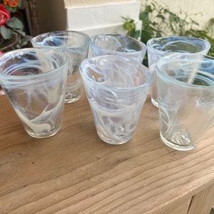 May include: Six clear glass drinking glasses with a white swirl pattern. The glasses are arranged in a row on a wooden surface.