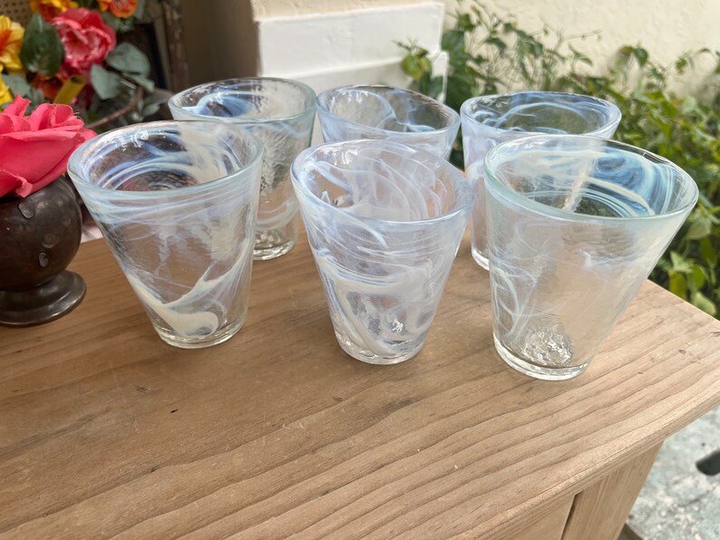 May include: Six clear glass drinking glasses with a white swirl pattern. The glasses are arranged in a row on a wooden surface.