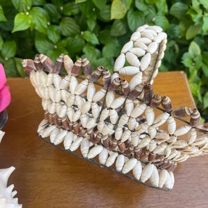 May include: A woven basket made from white and brown seashells. The basket has a handle and is made in a rectangular shape.