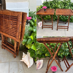 May include: A set of three bamboo folding tables. The tables have a natural brown finish and a slatted tabletop design. The legs are crossed for stability. One table is folded. The tables are surrounded by greenery and seashells.