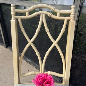 May include: A cream-colored wooden chair with a decorative back featuring a lattice design. The chair has a patterned seat cushion and a vibrant pink rose in a small metal container resting on the seat.