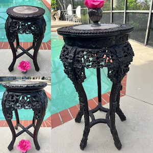 May include: Two black wooden side tables with intricate carvings and marble tops. The tables have three legs each and are decorated with floral patterns.