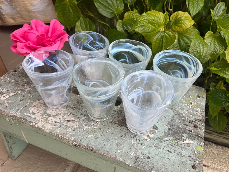 May include: Six clear glass tumblers with a swirling white pattern. The glasses are arranged in a circle on a weathered wooden surface.
