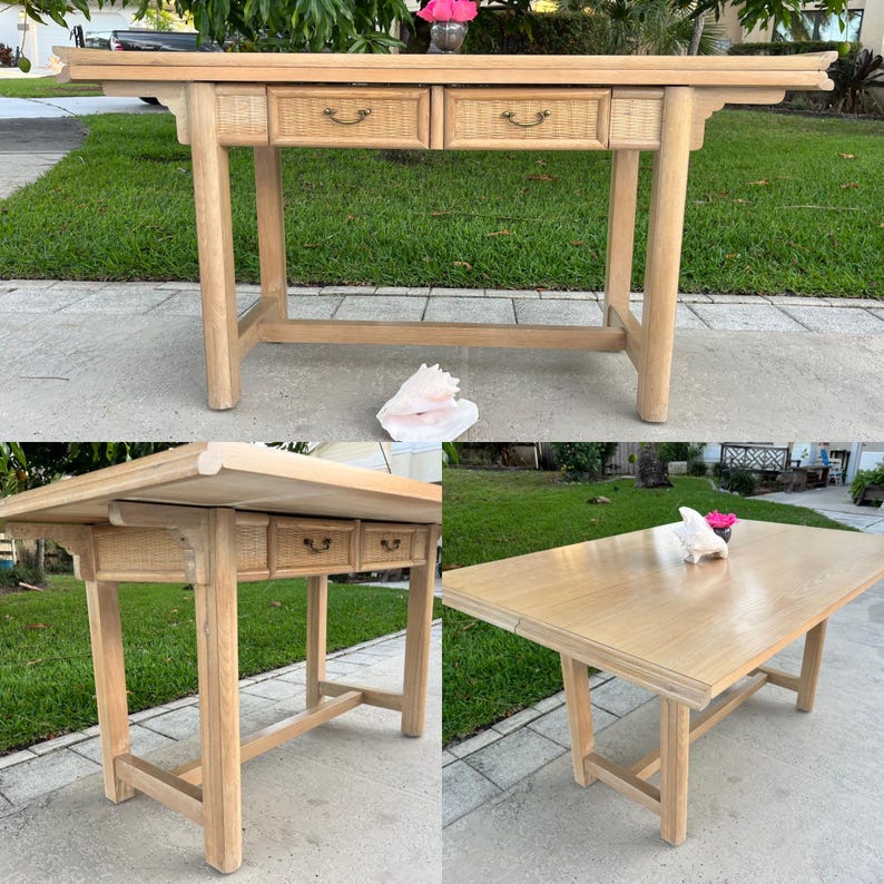 May include: Light wood console table with two drawers featuring woven rattan fronts and brass-toned pulls. The table has a rectangular top and four sturdy legs. A seashell and flowers are on the ground near the table.