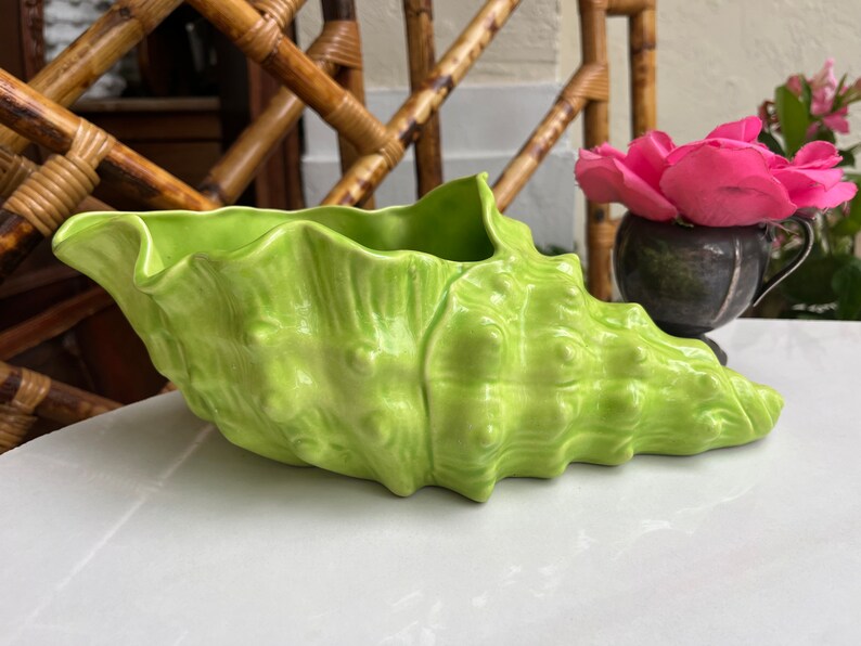 May include: A bright green ceramic seashell planter. The planter is shaped like a conch shell and has a textured surface.