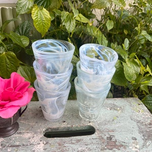May include: A set of four clear glass drinking glasses with a white marbled design. The glasses are stacked on top of each other.