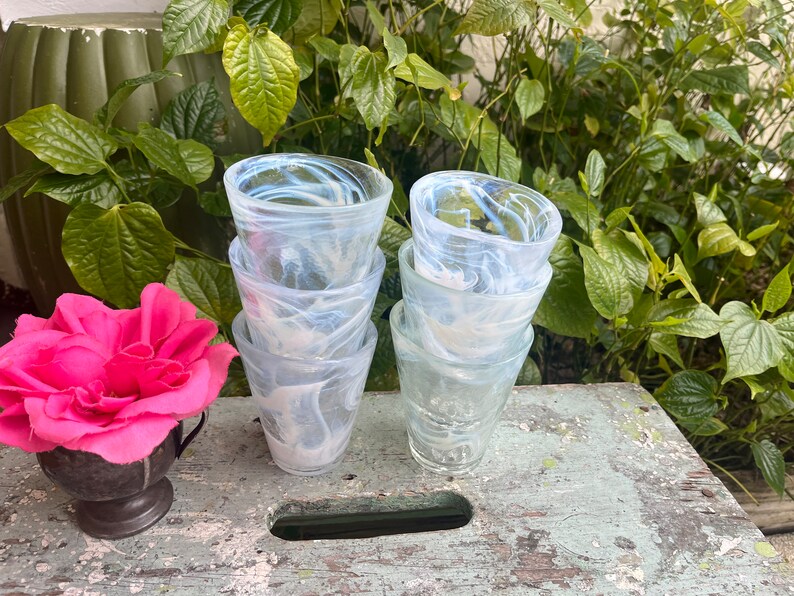 May include: A set of four clear glass drinking glasses with a white marbled design. The glasses are stacked on top of each other.
