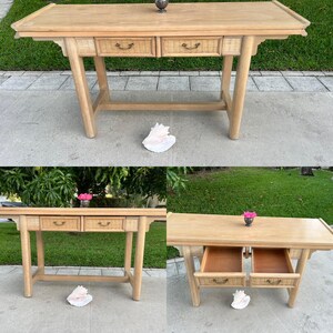 May include: Light wood console table with two drawers featuring woven rattan fronts and curved handles. The table has a rectangular top and angled legs. A decorative metal object sits on top.