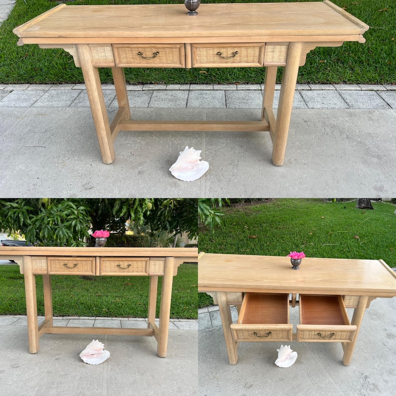 May include: Light wood console table with two drawers featuring woven rattan fronts and curved handles. The table has a rectangular top and angled legs. A decorative metal object sits on top.