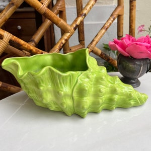 May include: A bright green ceramic seashell planter with a ruffled edge. The planter is sitting on a white surface.