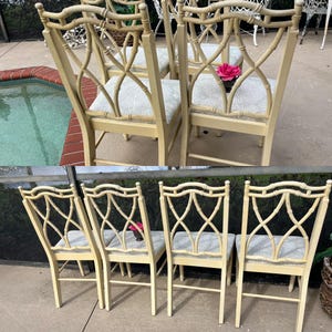 May include: A set of six cream-colored dining chairs with a bamboo-style frame and patterned seat cushions. The backs feature an intricate lattice design. A pink flower is placed on one chair.