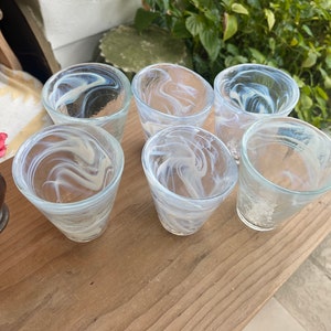 May include: Six clear glass drinking glasses with a white swirl pattern. The glasses are arranged on a wooden surface.