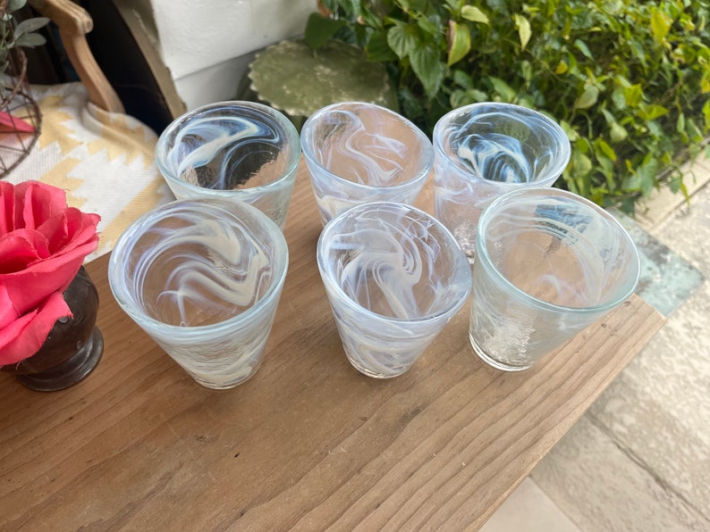 May include: Six clear glass drinking glasses with a white swirl pattern. The glasses are arranged on a wooden surface.