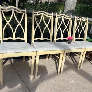 May include: Four cream-colored dining chairs with patterned gray seats. The chairs have a decorative back design and bamboo-style legs. A small silver vase with a pink flower sits on one of the seats.