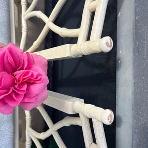May include: Off-white, bamboo-style headboard with a lattice design. The headboard has a distressed finish, with visible wear on the rounded end pieces. A bright pink flower is in the foreground.