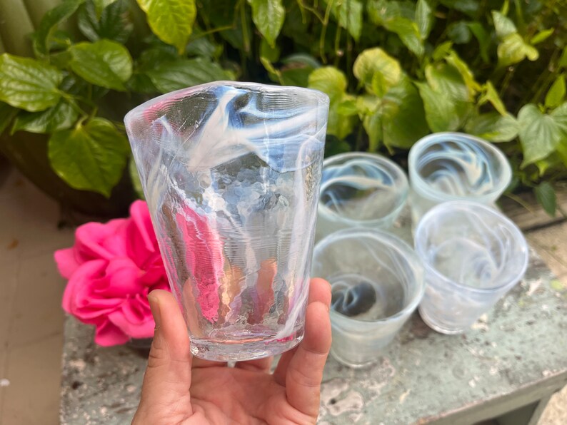 May include: Set of six clear glass tumblers with a white swirl design. The glasses are stacked on a table.