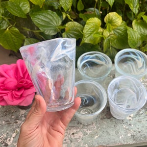 May include: Five clear glass cups with a white swirl design. The cups are arranged in a circle on a wooden surface.