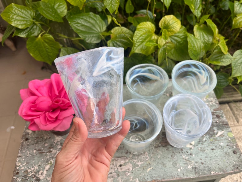 May include: Five clear glass cups with a white swirl design. The cups are arranged in a circle on a wooden surface.