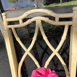 May include: Cream-colored chair back with a bamboo-style design. The back features a curved top and an X-shaped lattice pattern. A bright pink flower is visible at the bottom of the chair.