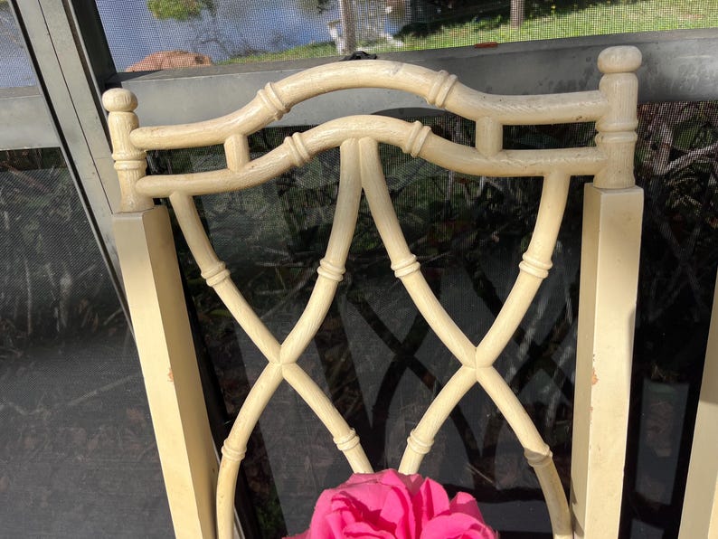 May include: Cream-colored chair back with a bamboo-style design. The back features a curved top and an X-shaped lattice pattern. A bright pink flower is visible at the bottom of the chair.