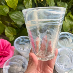 May include: Set of four clear glass drinking glasses with a white swirl pattern. The glasses are stacked on top of each other.