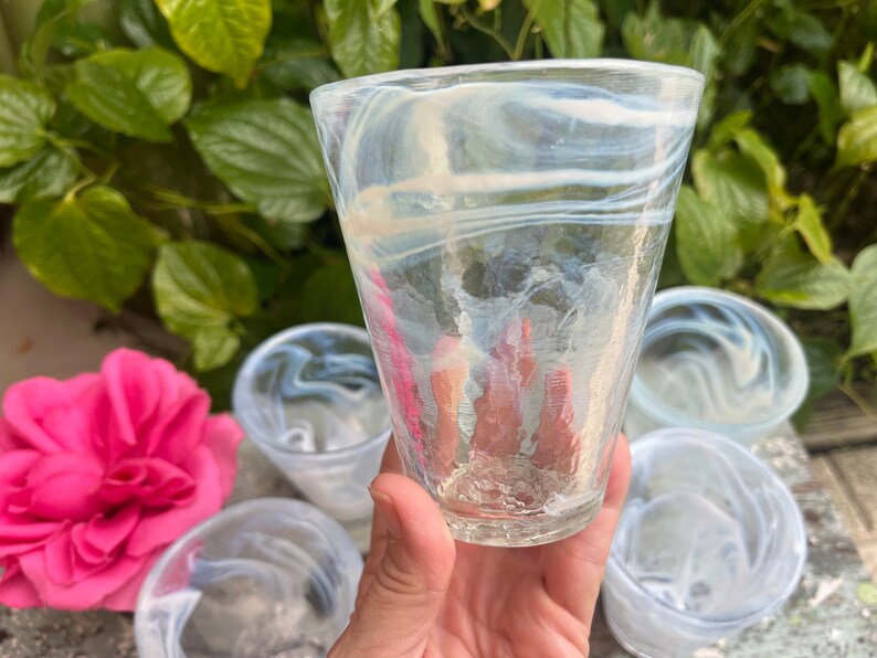 May include: Set of four clear glass drinking glasses with a white swirl pattern. The glasses are stacked on top of each other.